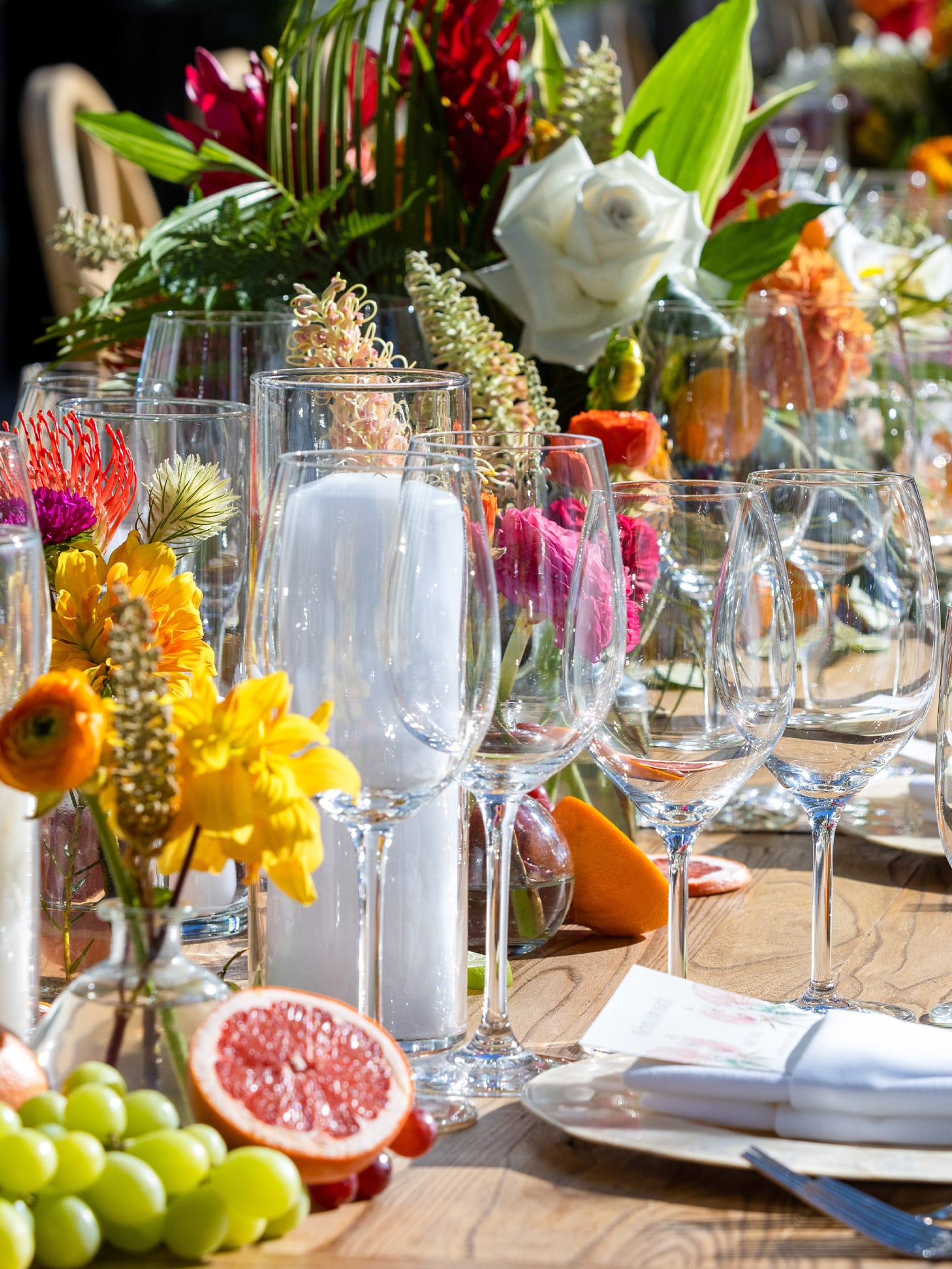 Colorful summer BBQ table with tropical flowers, citrus accents, glassware, and outdoor place settings